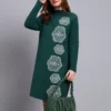 Woman in green knit winter dress with vertical white geometric embroidery, high neck, and full sleeves.