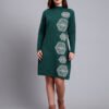 Woman in green knit winter dress with vertical white geometric embroidery, high neck, and full sleeves.