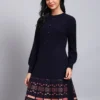 Woman wearing navy knit winter dress with pastel pink patterned hem, button-front bodice, and long sleeves