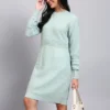 Woman in pistachio green textured knit midi winter dress with round neck, long sleeves, and front pocket.